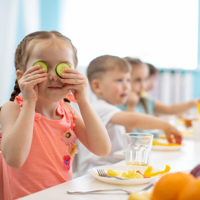 Funny kid eating healthy food in kindergarten or daycare