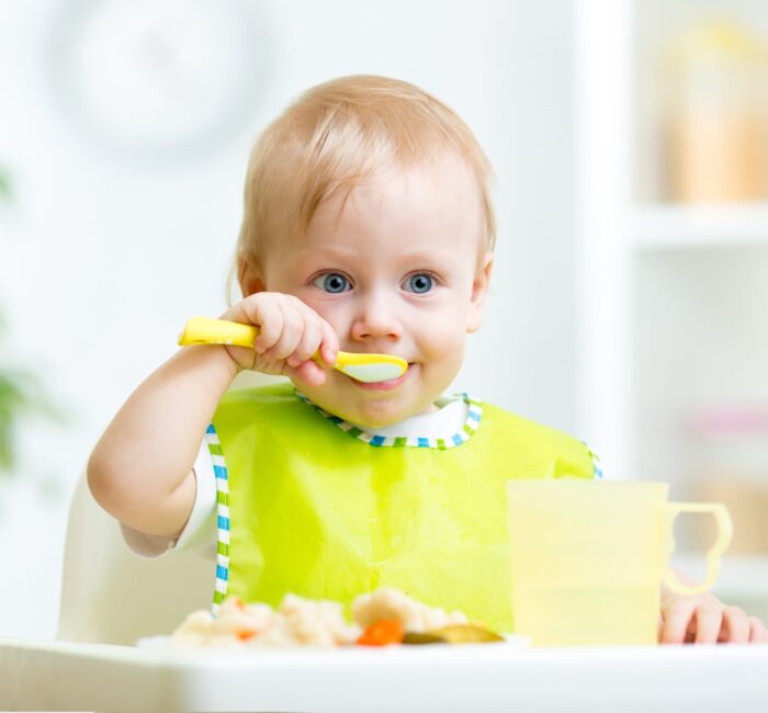 kid eating healthy food with a spoon at kitchen